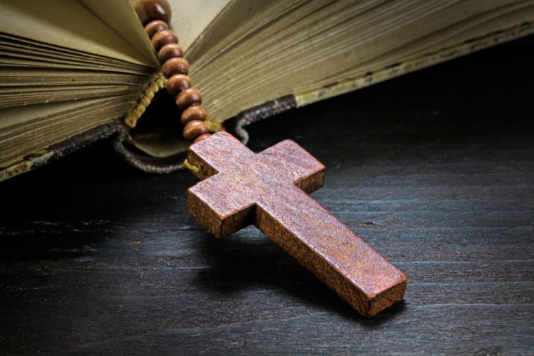 catholic wooden rosary beads with cross in an old book on dark rustic wood, religious symbol concept, toned with color filter, selected focus on christ, narrow depth of field